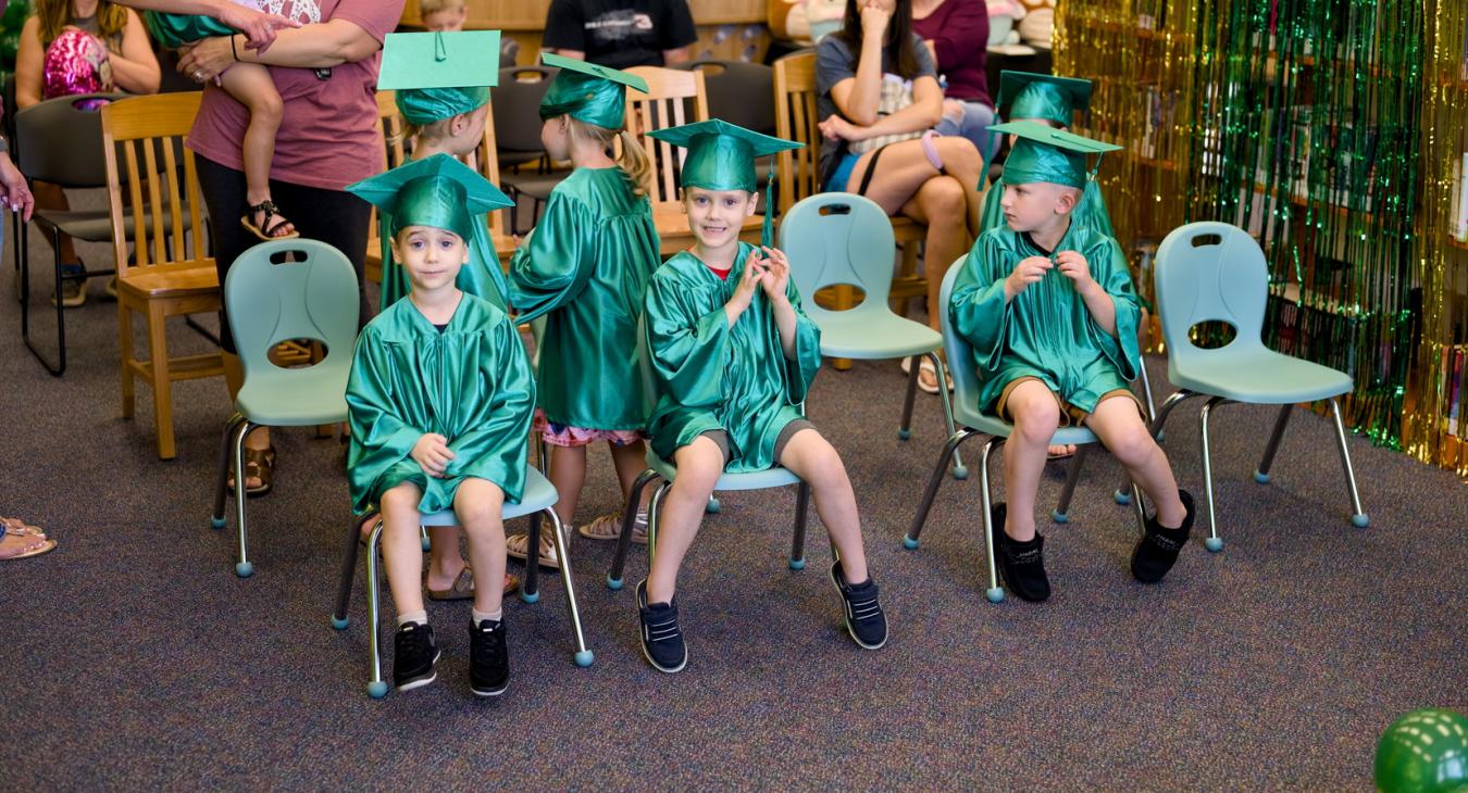 children in green caps and gowns sitting on chairs